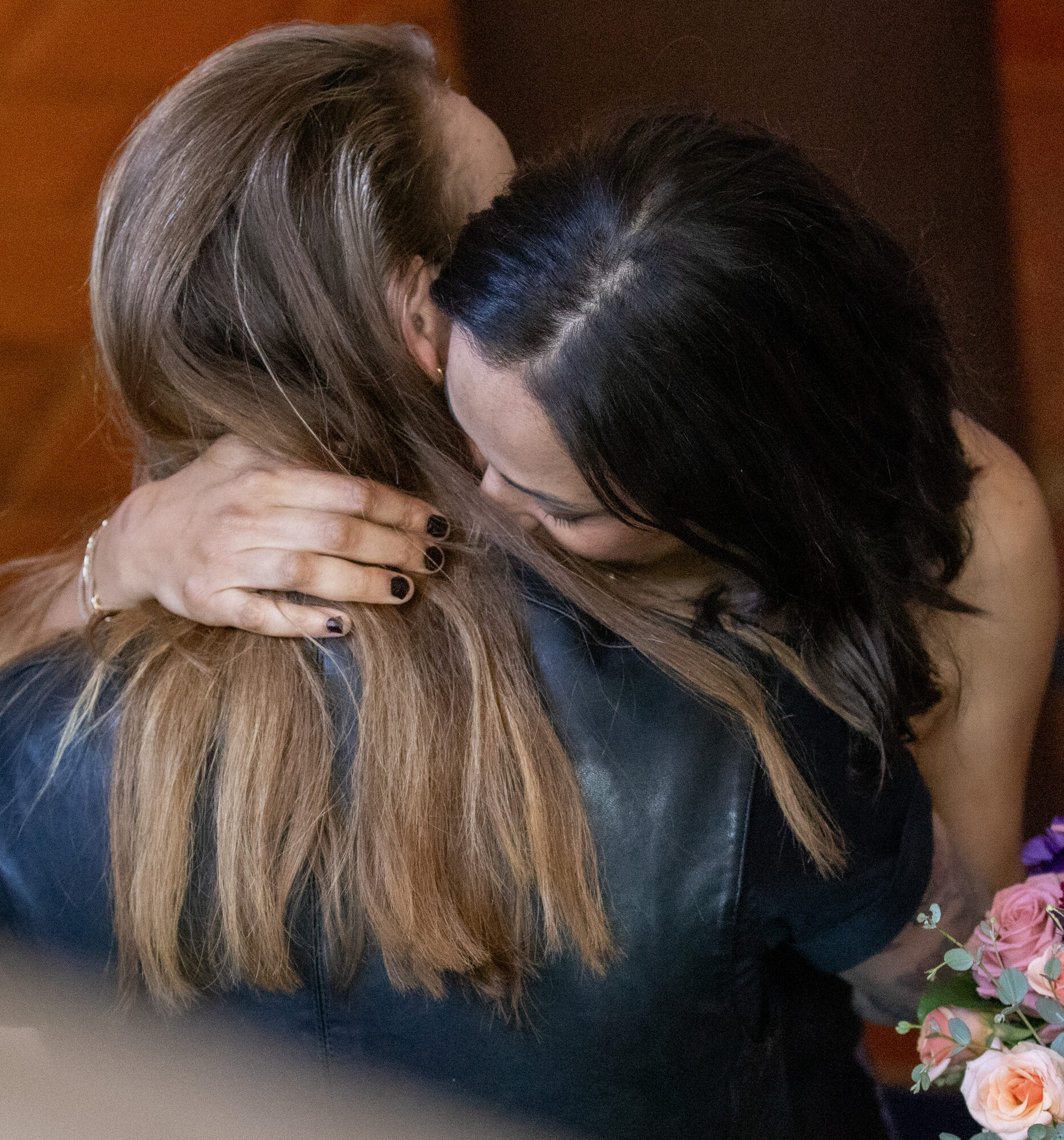 Two women in a close embrace, one holding a bouquet