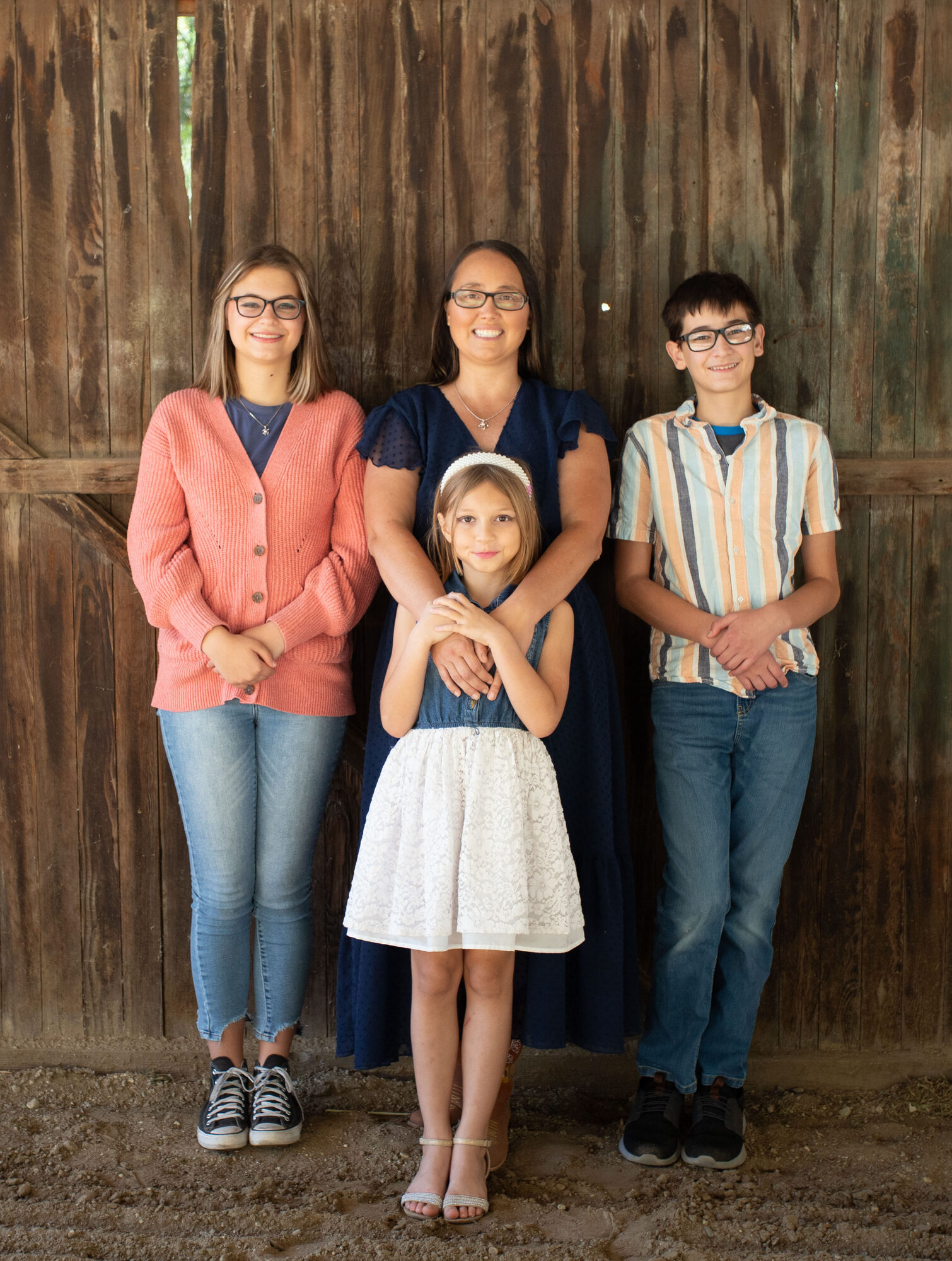 A mother and her three children in front of a weathered barn door